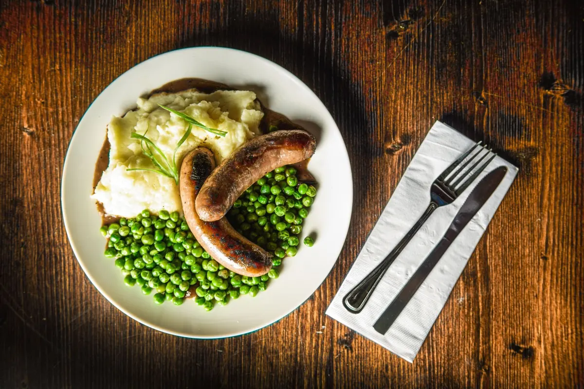Bangers, mash and peas on a wood table