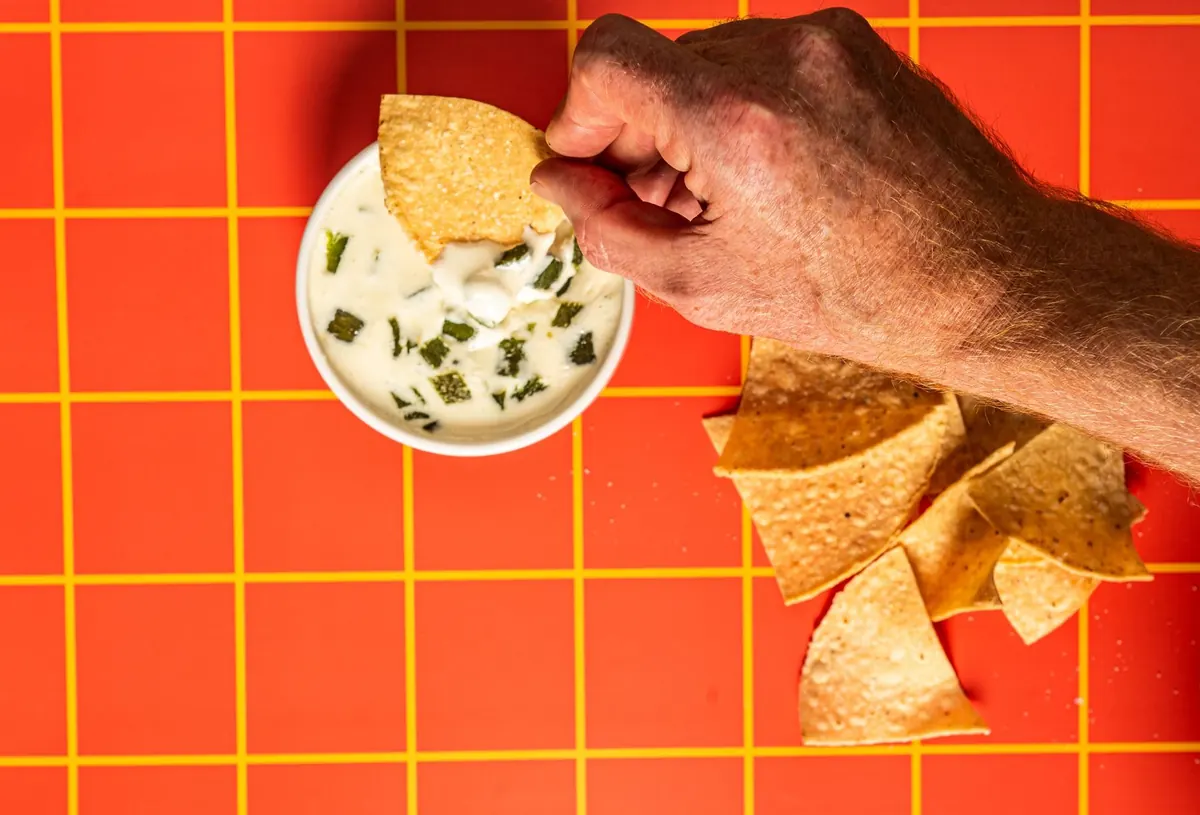 Hand dipping a chip into crema on an orange grid