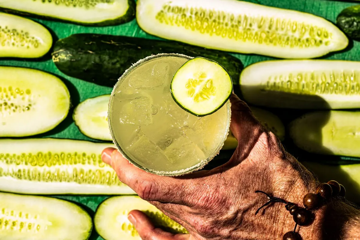Cucumber margarita held over sliced cucumbers