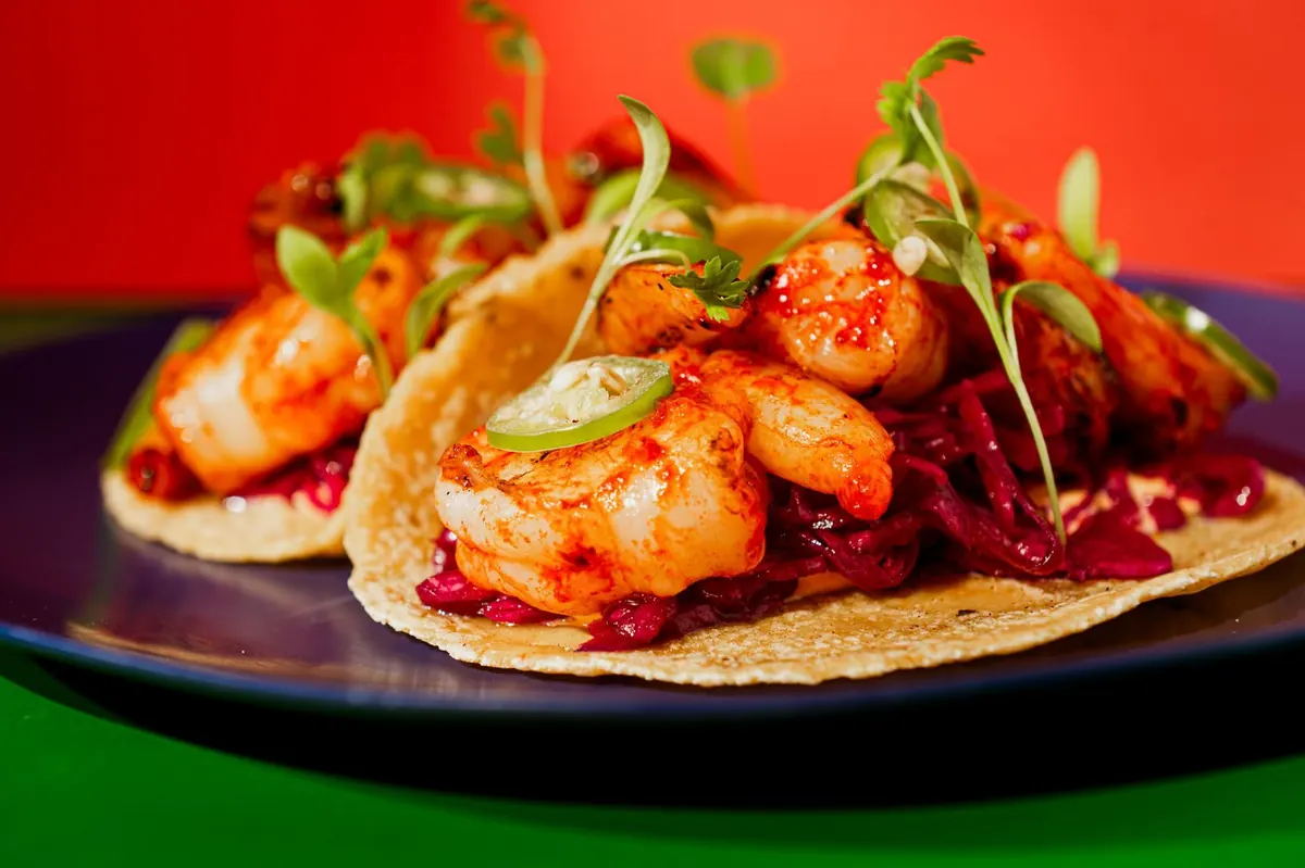 Shrimp tacos on a blue plate against orange and green